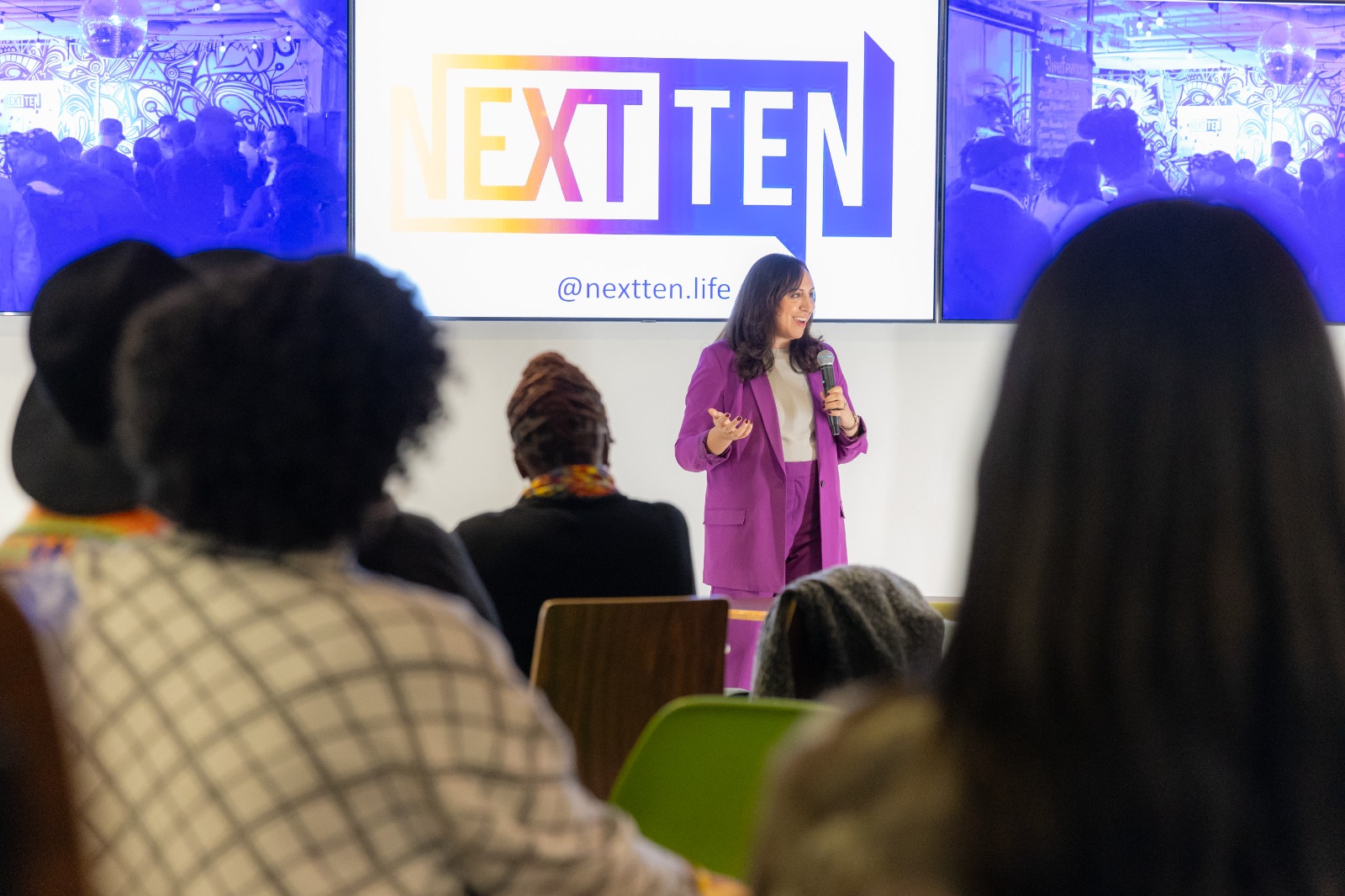 A speaker presenting to a seated audience at a NEXT TEN experience